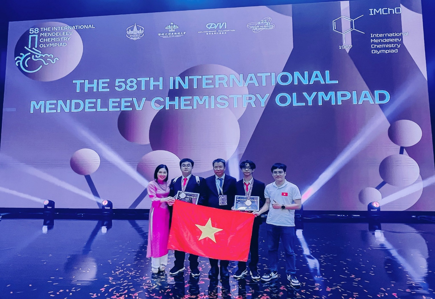 A group of people holding a flag and awards

Description automatically generated