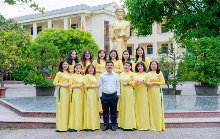 A group of women in yellow dresses standing in front of a statue Description automatically generated